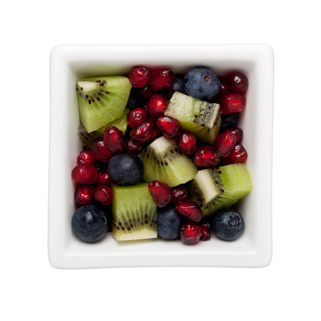 Pomegranate arils, blueberries and diced kiwifruit in a square bowl isolated on white backgroundの写真素材
