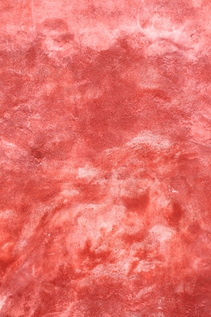 Architectural detail of plastered wall with uneven red paint.