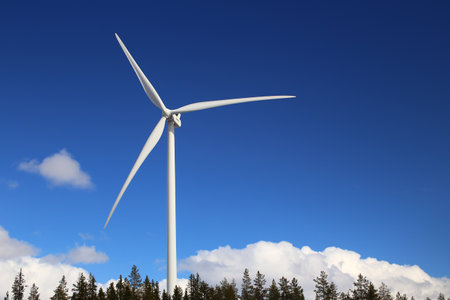 Wind turbine over forest and clouds with blue sky.の写真素材