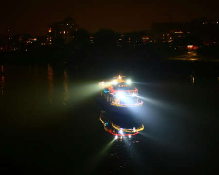 Small ship on a river with search lights and illumination in the night.の写真素材