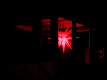 Red Moravian star hanging in a dark patio.の写真素材