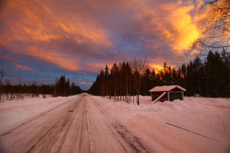 Winter road and old rural shed under orange cloudscape in the evening.の写真素材