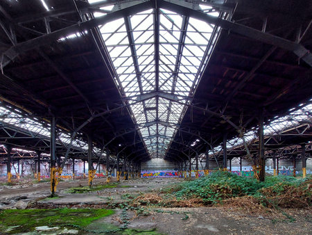Huge abandoned factory with damaged skylight roof and blackberry bushes growing inside.の写真素材