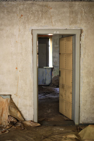 Open doorway leading into a decayed interior with peeling walls and scattered debris on the floor.の写真素材