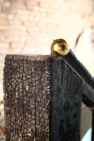 Burnt wood railing with brass sphere detail in softly lit indoor setting.の写真素材