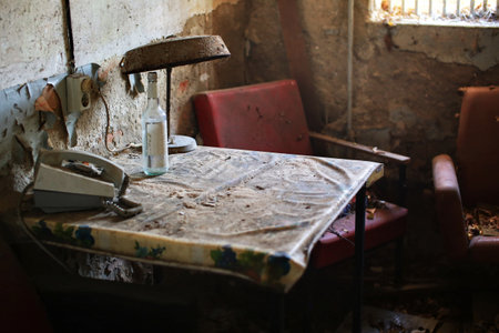 Dusty table with a rotary phone, empty bottle, and rusted lamp in an abandoned interior.の写真素材