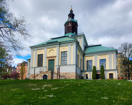Baroque style Kungsholm Church in Stockholm with green copper roof in a quiet park under a cloudy spring sky.の写真素材