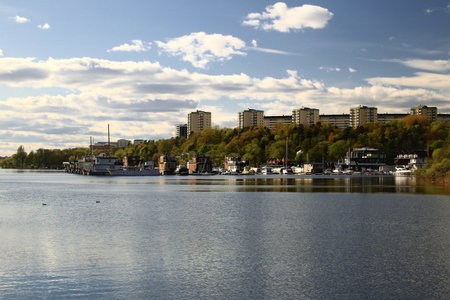 Residential buildings of Stockholm across water with tree-lined shoreline under a partly cloudy spring sky.の写真素材