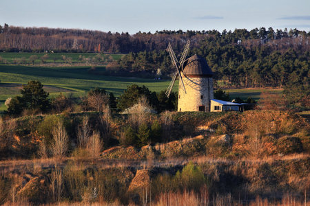 Stone windmill sitting on a gentle slope surrounded by trees in warm evening light.の写真素材