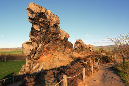 Sandstone rock face of Teufelsmauer, Germany, catching warm evening light along narrow dirt path.の写真素材