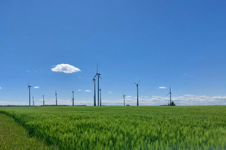 Wind turbines field stretching across a wide green plain beneath a clear blue spring sky.