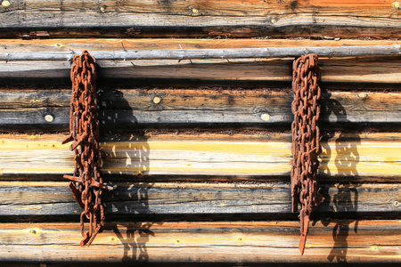 Rusted chains hang from a wooden cabin wall, casting long shadows in the morning light.の写真素材