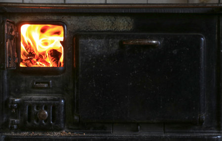Full view of cast iron stove with fire glowing in left chamber and closed compartment on right.の写真素材