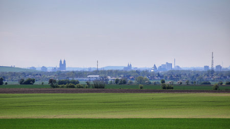 Distant city skyline of Magdeburg seen beyond wide green farmland under a clear spring sky.の写真素材