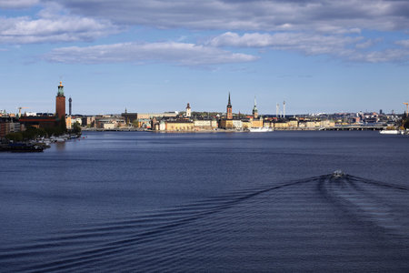 Boat leaves wake crossing Stockholm waterfront with skyline and town hall in background.の写真素材