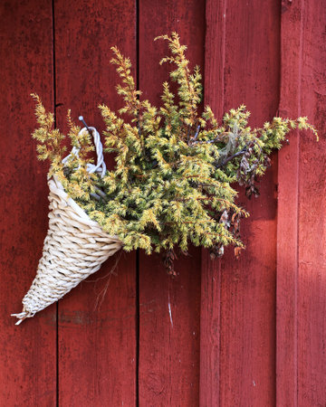 Close-up woven bouquet hanging on rustic red cabin wall with dried juniper foliage.の写真素材