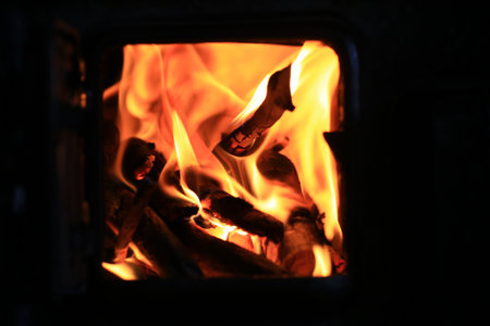 Close-up of intense flames and wood burning inside dark iron stove with visible inner firebox.の写真素材