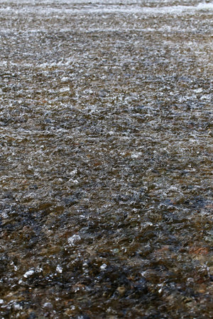 Flowing shallow water with ripples and rocks underneath.