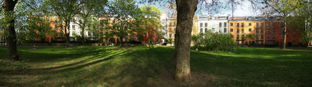 Trees cast shadows across a residential park in Stockholm bordered by colorful facades in early spring.の写真素材