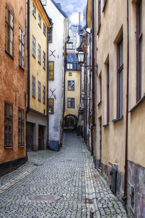 Narrow alley with historic ocher buildings and cobblestone path leading through old town in Stockholm.の写真素材