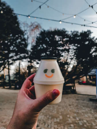 A man holds a paper cup with a smiley face in his hand.