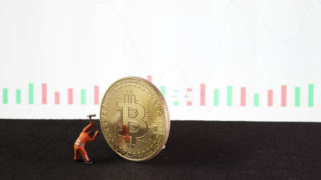 A mining miniature is taking profit from bitcoin trading on stock background. conceptual image for...