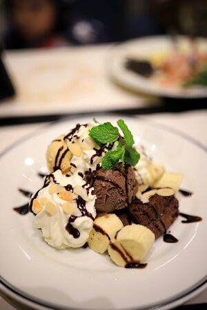 Chocolate ice cream and sliced bananas Garnish with mint leaves. With white mousse and sliced almonds in a white plate Topped with chocolate sauce to look delicious. Selective focus.の写真素材