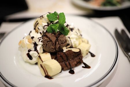 Chocolate ice cream and sliced bananas Garnish with mint leaves. With white mousse and sliced almonds in a white plate Topped with chocolate sauce to look delicious. Selective focus.の写真素材
