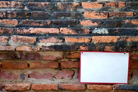 Old red brick wall Full of moss stains There is a white sign with a red border placed in the lower right corner.の写真素材
