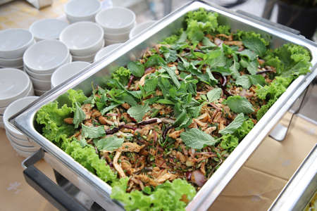 Larb Moo, sprinkled on top with mint leaves in buffet line. The container is a rectangular stainless steel tray with small white cups arranged on the side. Selective focus.の写真素材