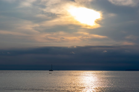 Evening sea pictures cloudy sky the sun is about to set I could see a sailboat holding sails in the distance. small in picture The sunlight reflects on the water surface.の写真素材