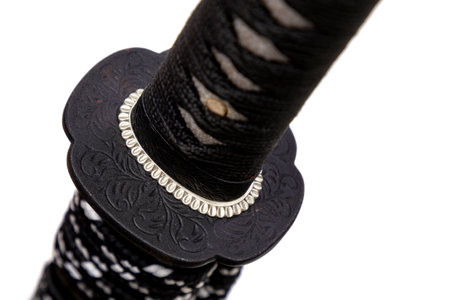 Close up shot of Tsuba - hand guard of Japanese sword made by steel isolated in white background. The sword handle wrapped by black silk cord and white ray skin. Selective focus.の写真素材