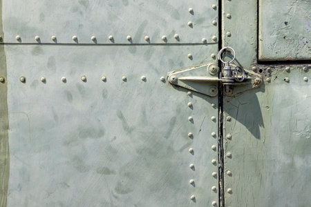 The exterior wall surface of a very old military green military helicopter. There is a door hinge on the right side of the picture. in the bright sunlight during the dayの写真素材