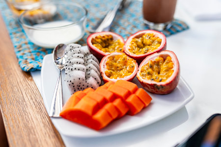 A shallow focus shot of a white plate of fruit at breakfast in a hotel. Dragon fruit, papaya. The...