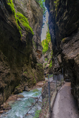 Narrow walkway carved into the cliffside along a turquoise stream inside Partnachklamm Gorge, Garmisch-Partenkirchen, Bavaria. A stunning natural passageway through dramatic alpine rock formations.の写真素材