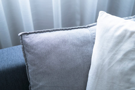 Close-up of cushions on cozy grey sofa. Modern interior of living room. with large window and sheer...