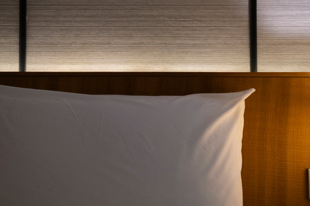 Modern Japanese style bedroom headboard with bed and pillows for sleeping and resting in a dim atmosphere with a bedside light on. Accommodation, hotel.の写真素材