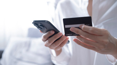 Close up female hands holding credit card and smartphone, young woman paying online, using banking...