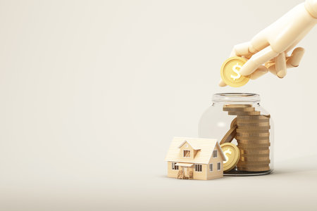 A wooden hand drops a gold coin into a glass jar filled with stacked coins beside a small house model, symbolizing savings for home ownership, 3d rendering.の写真素材