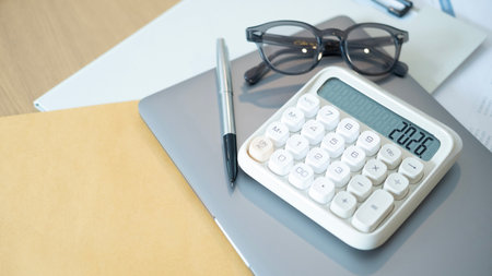 A white calculator with glasses and silver pen on laptop over reports showing charts and numbers symbolizing financial planning stability and concepts of money security.の写真素材