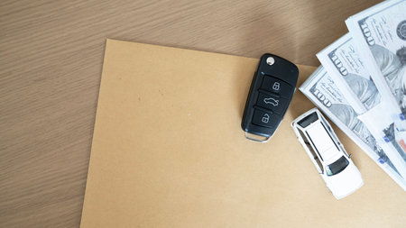 Car financing concept with car key and cash dollars on brown document envelope, symbolizing vehicle...