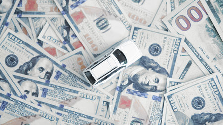 A small white toy car and a car key placed on US dollar bills symbolizing car purchase cost, auto loan payments and financial decisions in vehicle ownership.の写真素材