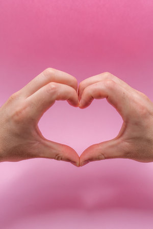Isolated white man's hands on a pink background. Romantic heart-shaped gesture. Horizontal color photograph, for valentine's dayの写真素材