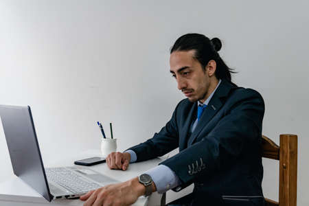 businessman at a conference on his home computer wearing a monochrome blue suit and titanium watch, with a cell phone on the table and some pens. Labor dayの写真素材