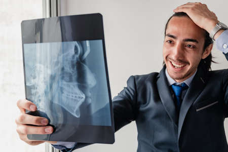 orthodontist looking at a dental profile x-ray with hand on forehead showing concern and laughter,...