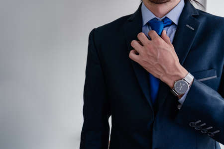 businessman adjusting his blue tie for his monochromatic suit with his veined and very masculine hand, showing off his titanium watch.の写真素材