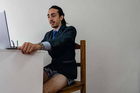 man working from home looking at his computer, wearing a monochromatic blue suit with no pants, copy-space on the right-hand sideの写真素材