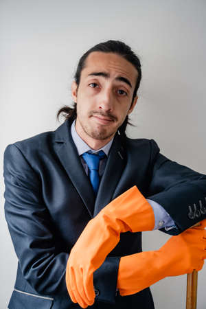 businessman holding household cleaning supplies, face of resignation for not knowing how to clean,...