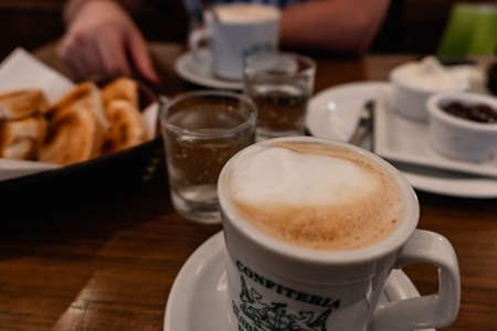 coffee with foam, accompanied by toast with cream cheese and jam, cafeteria table ready for consumption.の写真素材