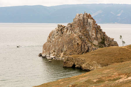 Figures of 2 people on Shamanka Rock and a boat near Khuzhir, main village on Olkhon Island in Lake Baikal in eastern Siberia. The photo was taken in the summer in July.の写真素材